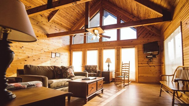 A cozy cabin interior with wooden walls and ceiling, a sofa, a chair, a small table, and a TV mounted on the wall. - Lakeside 3 bedroom chalet with hot tub!! (Byrdstown)