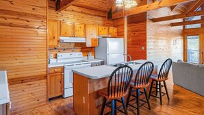 A cabin interior with wooden walls, a kitchen with white appliances, and a dining area with four chairs. - Lakeside 3 bedroom chalet with hot tub!! (Byrdstown)
