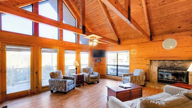 A spacious living room with wooden floors, a fireplace, and large windows. - Lakeside 3 Bedroom Chalet with a hot tub! (Byrdstown)