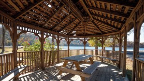 A wooden gazebo with a picnic table, surrounded by a wooden deck and railings, overlooking a lake. - Lakeside 3 Bedroom Chalet with a hot tub! (Byrdstown)