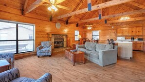 A spacious cabin with a wooden interior, a fireplace, a dining area, and a kitchen. - Lakeside 3 Bedroom Chalet with a hot tub! (Byrdstown)
