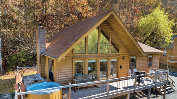 Een houten chalet met een jacuzzi en terras, omringd door bomen.