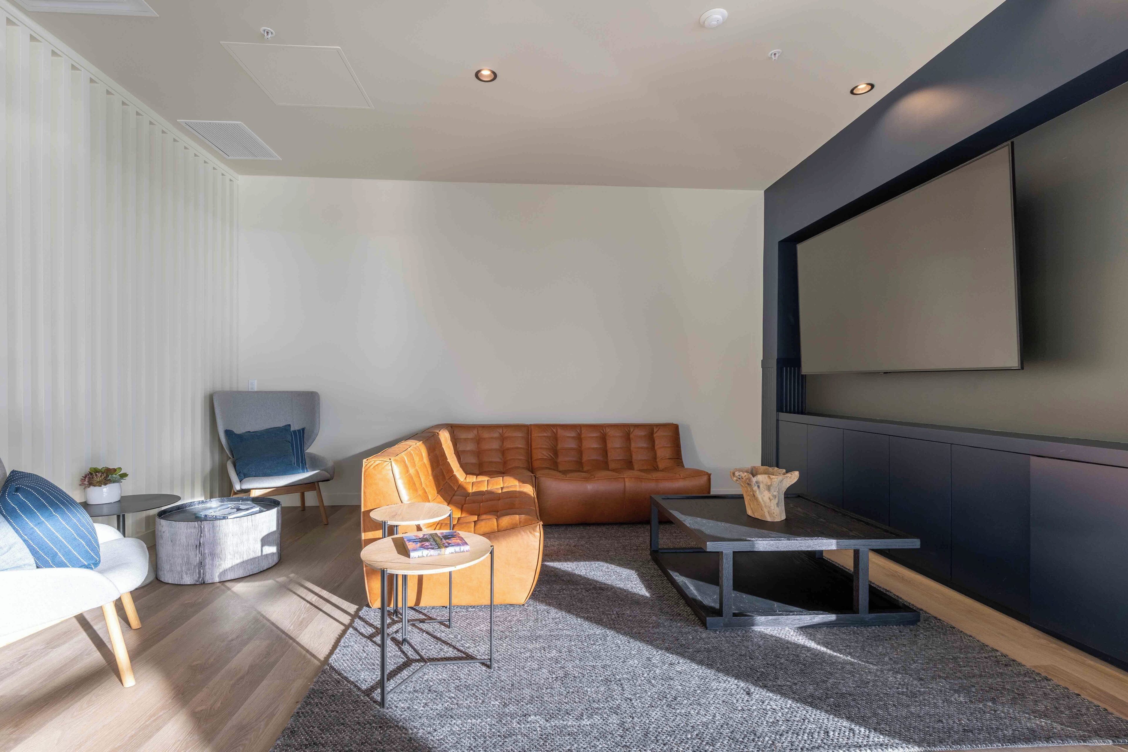 Ein modernes Wohnzimmer mit einem Ledersofa, einem runden Couchtisch, einem kleinen Beistelltisch und einem flachbildfernseher an der Wand.