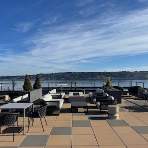A terrace with outdoor seating, a view of the water, and a distant forested area. - Marina Square Suites (Bremerton)
