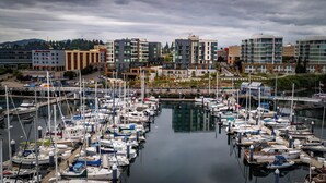A marina with numerous boats docked, surrounded by modern buildings and a clear sky. - Marina Square Suites (Bremerton)