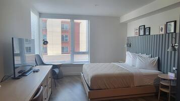 Een slaapkamer met een bed, bureau, stoel en een raam met luxaflex.