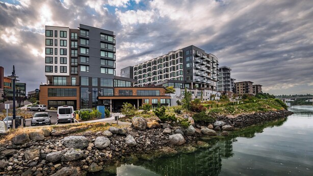 A modern building with multiple floors, a parking area, and a waterfront view. - Marina Square Suites (Bremerton)