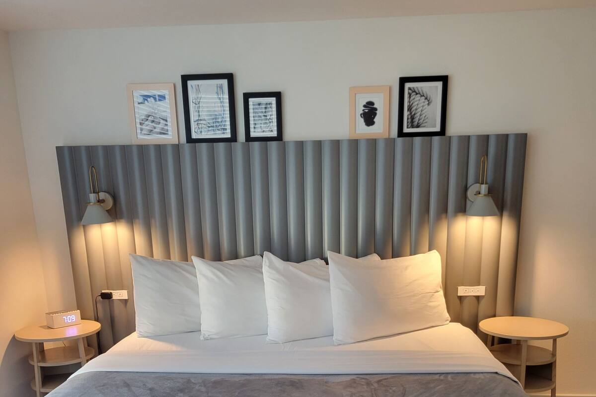 A hotel room with a large bed, a headboard with framed artwork, bedside lamps, and a small table.