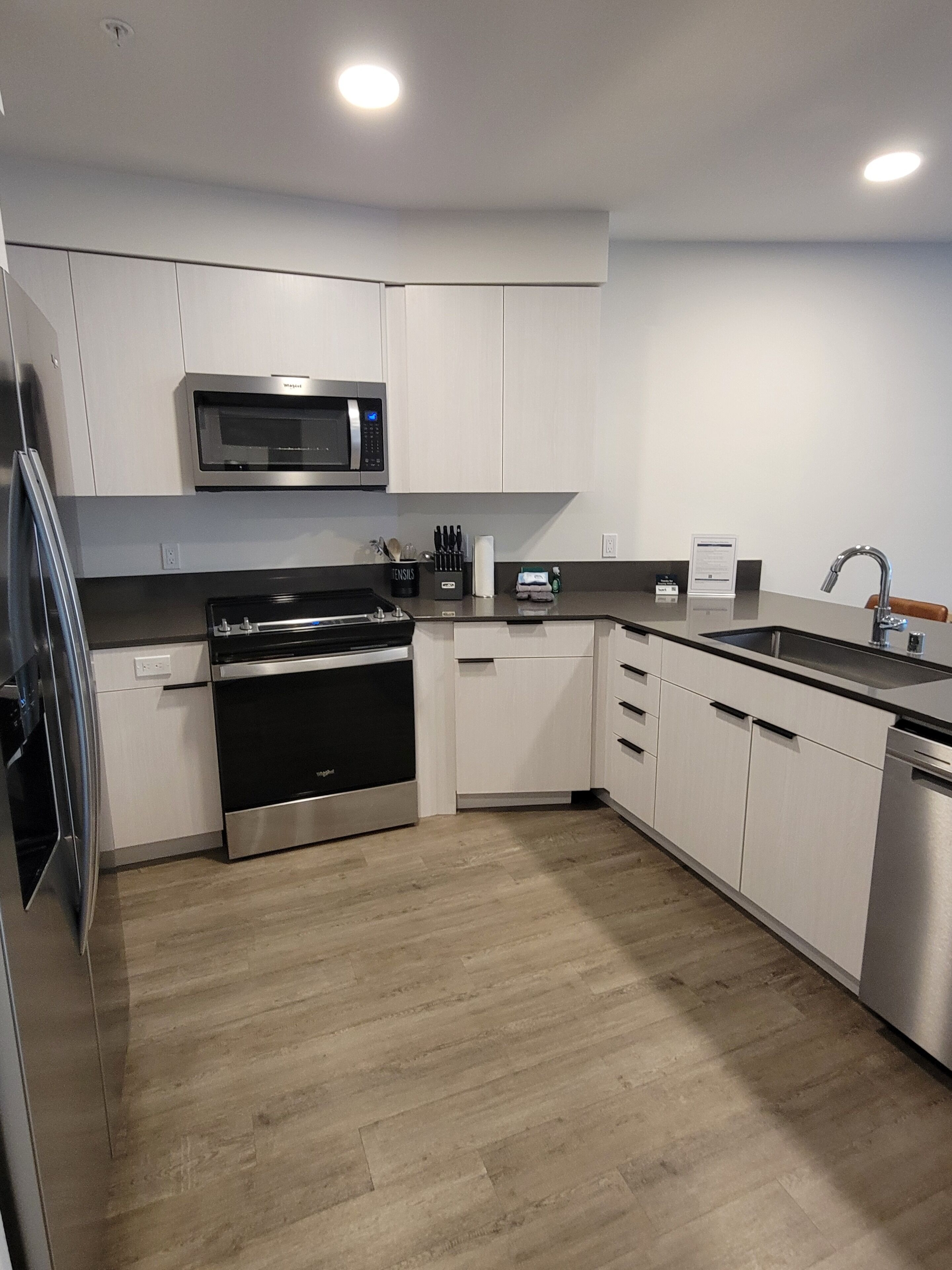 A modern kitchen with stainless steel appliances, white cabinetry, and a wooden floor.