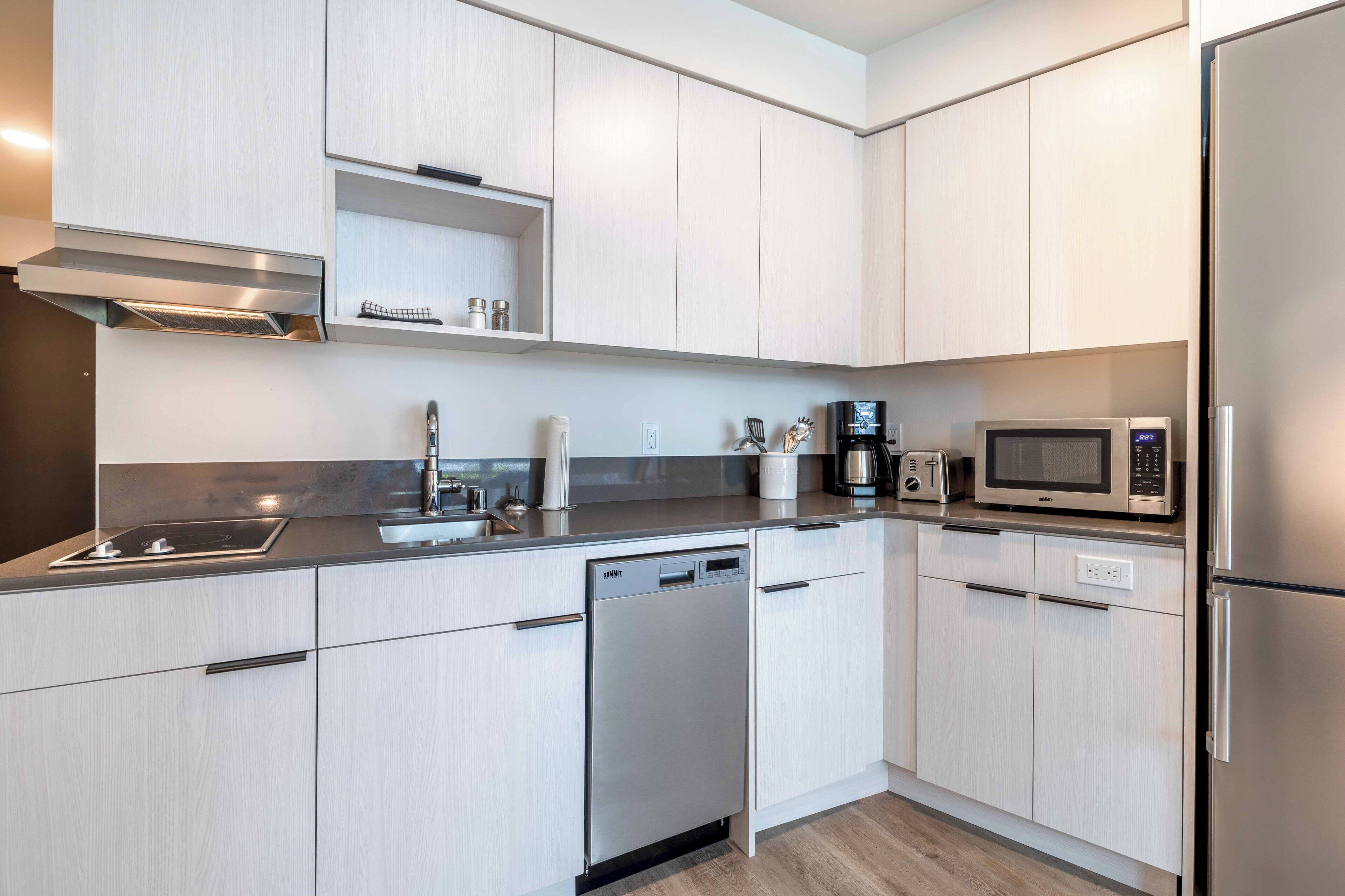 A modern kitchen with light wood cabinets, stainless steel appliances, and a built-in dishwasher.