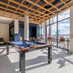 A pool table in a modern room with large windows and a view of the city. - Marina Square Suites (Bremerton)