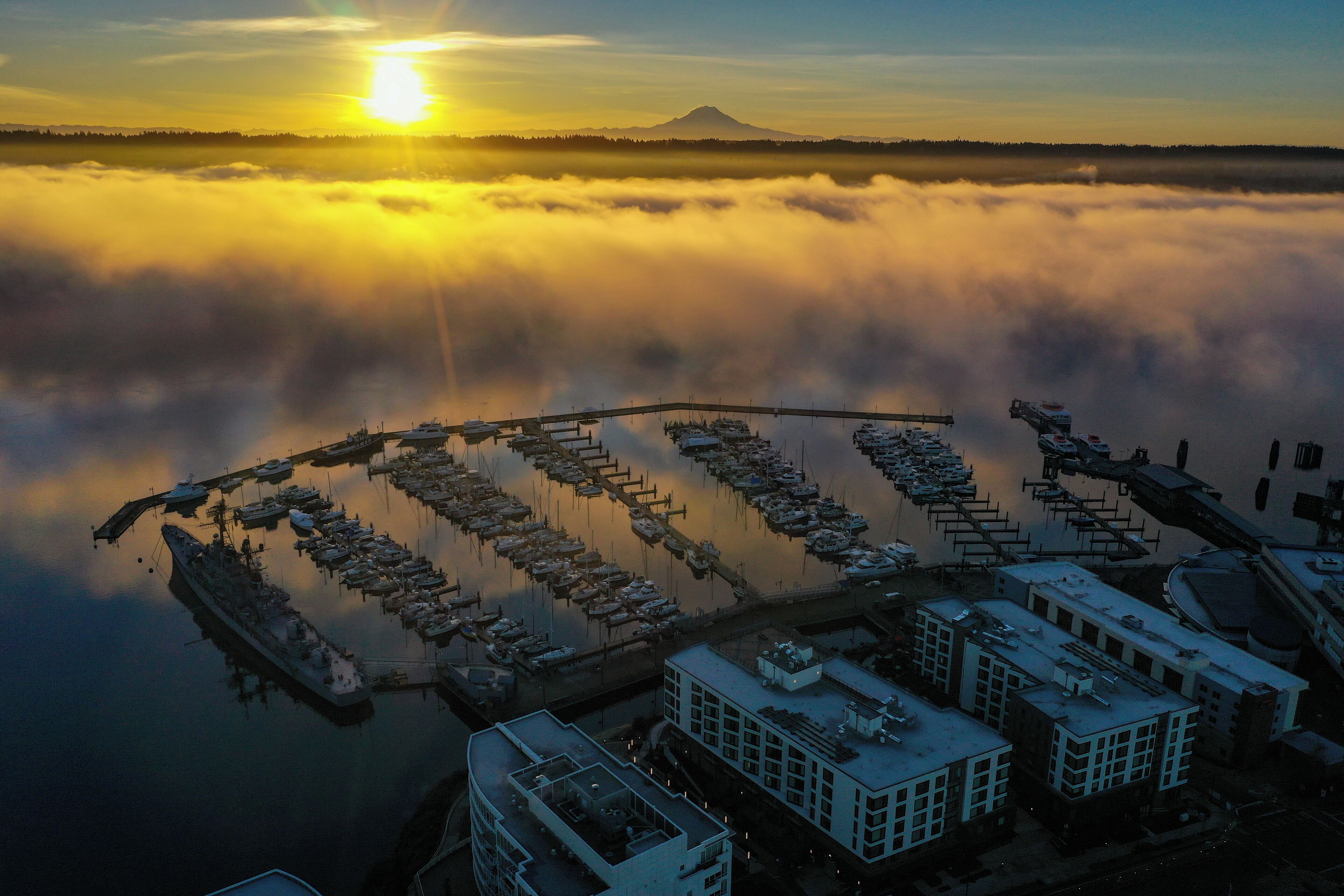 Vue aérienne d’une marina où sont amarrés des bateaux, le tout enveloppé de brouillard, avec une montagne en arrière-plan.