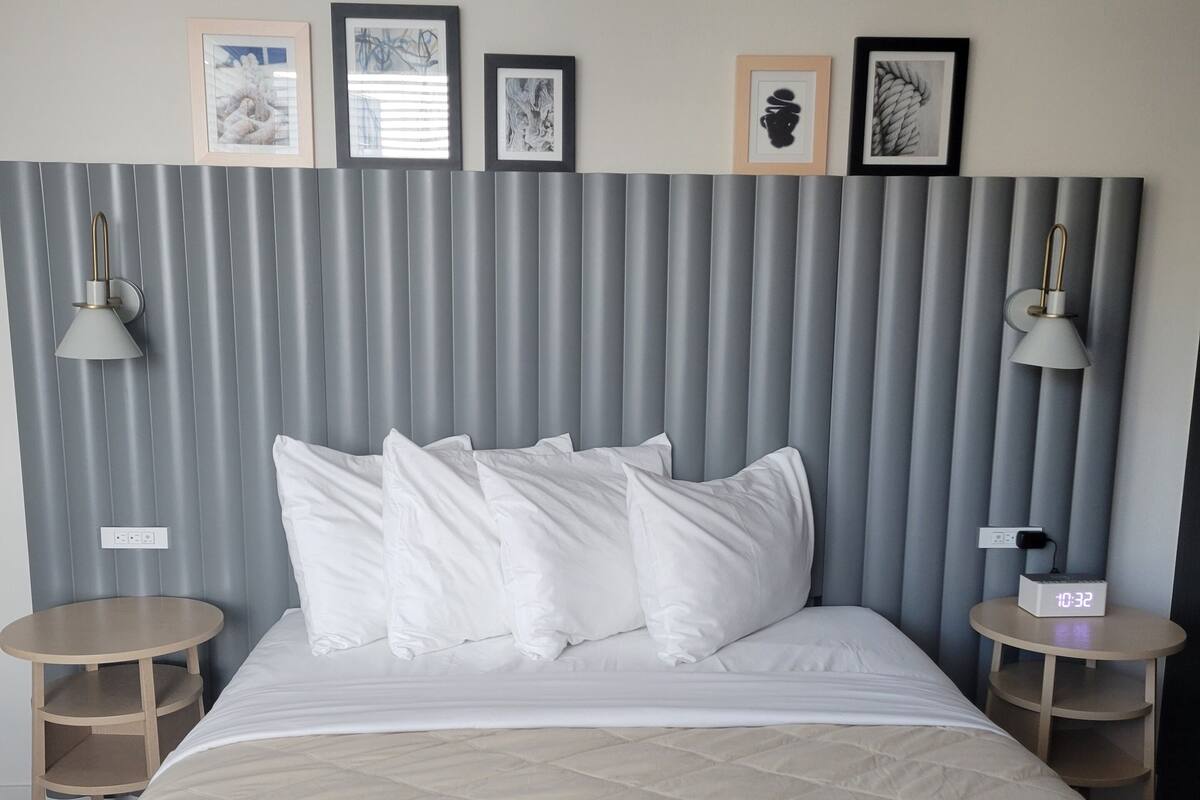 A bed with a quilted headboard, two bedside tables, and four framed pictures on the wall.