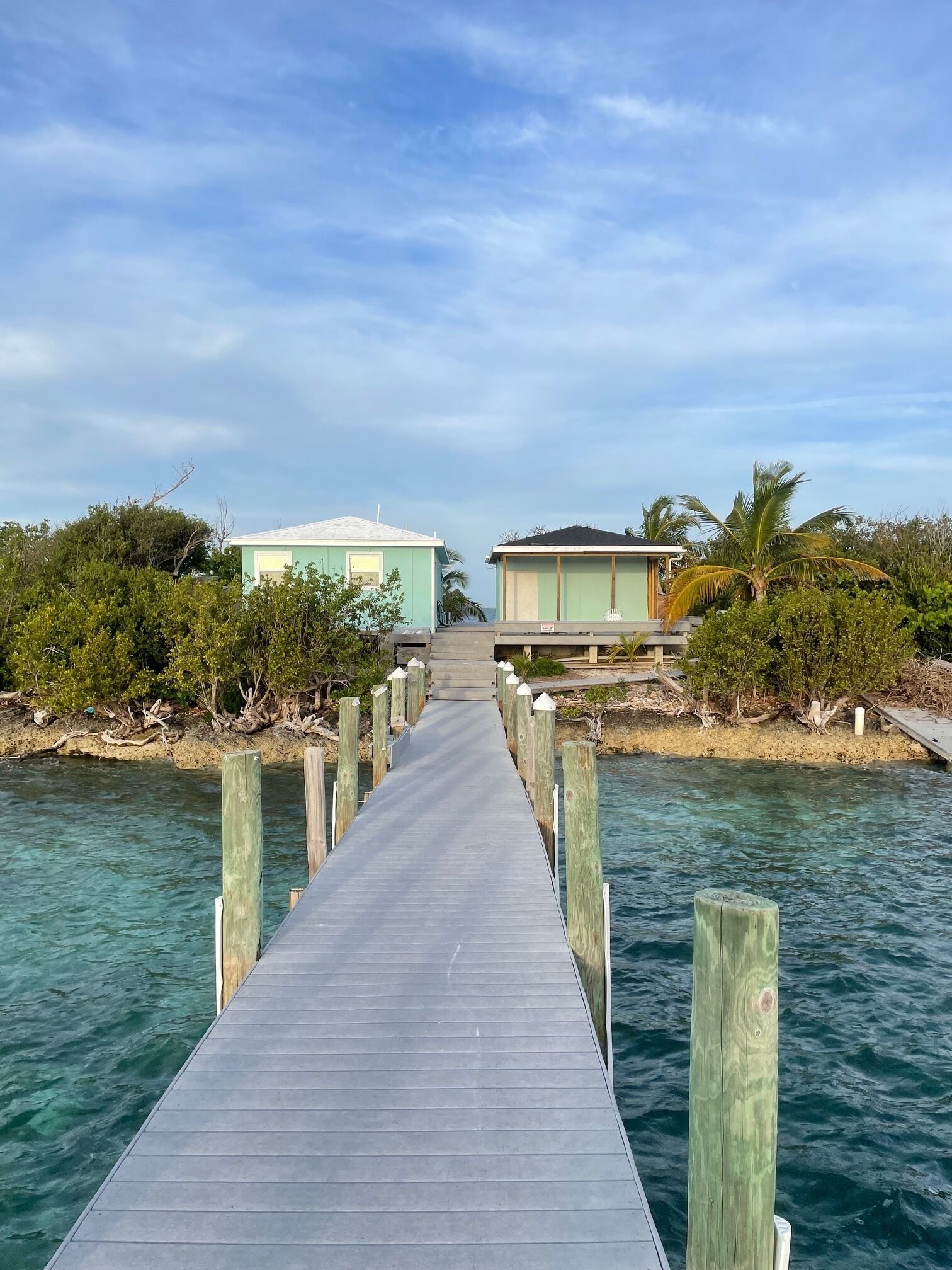 A wooden pier leading to two small buildings, surrounded by water and greenery.