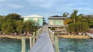 A wooden pier leading to two small buildings, surrounded by water and greenery.