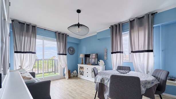 Quarto com mesa de jantar, cadeiras, televisão e varanda com cortinas.