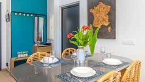 Un comedor con una mesa redonda dispuesta para cuatro personas, una pared de acento color verde azulado, un mapa de Francia y un aparador con espejo.