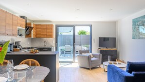 Una cocina moderna con armarios de madera, un comedor con mesa de vidrio y una sala de estar con sofá azul y televisor.