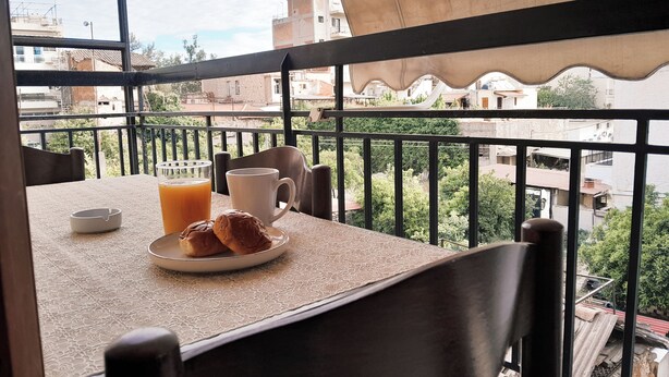 A balcony with a table set for breakfast, including a plate with pastries and a glass of orange juice, and a white mug.