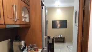 A kitchen with a stove, oven, and refrigerator. There is a dining area with a table and chairs. The room has wooden cabinets and a tiled floor.