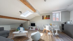 A modern living room with a loft-style ceiling, a dining area with white furniture, and a kitchen with a grey countertop. - Le Jarente - Appt pour 2 centre de Lyon (Lyon)