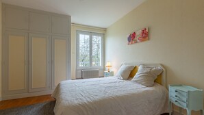 Quarto com cama, mesa de cabeceira, cômoda e janela.