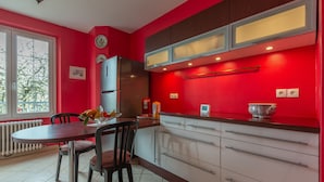 Cozinha moderna com paredes vermelhas, geladeira de aço inoxidável e área de refeições com mesa e cadeiras.