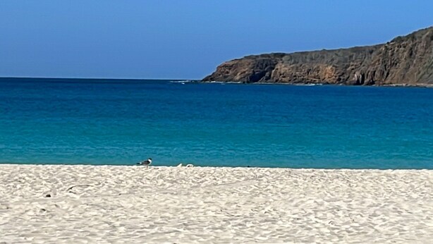 A beach with clear blue water and a rocky cliff in the background.