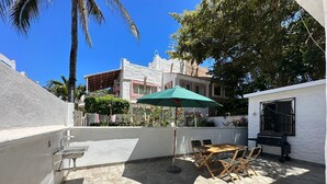 A patio with a table and chairs, a green umbrella, and a barbecue grill. - Acogedora casa dentro de fraccionamiento a orilla de la playa (Mazatlán)