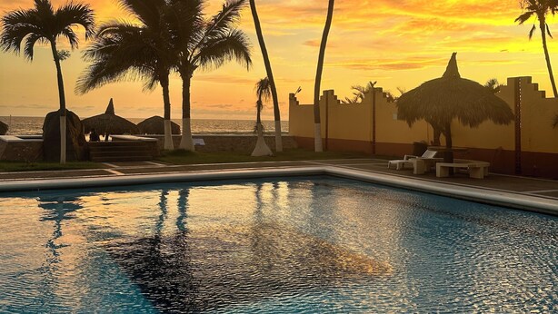 A swimming pool with palm trees and a sunset in the background. - Acogedora casa dentro de fraccionamiento a orilla de la playa (Mazatlán)