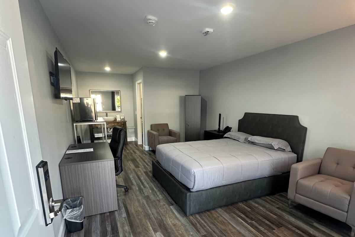A modern hotel room with a large bed, a desk, a chair, and a wardrobe.
