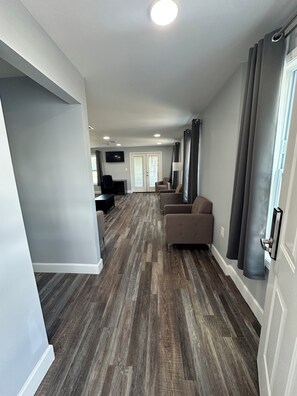 A spacious hallway with a wooden floor, grey walls, and a door leading to a room with a television.
