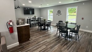Una habitación amplia con suelo de madera, un área de cocina y un comedor con múltiples mesas y sillas.