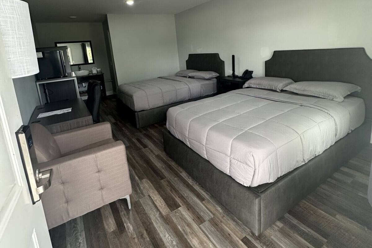 A hotel room with a large bed, a smaller bed, a desk with a computer, and a chair.