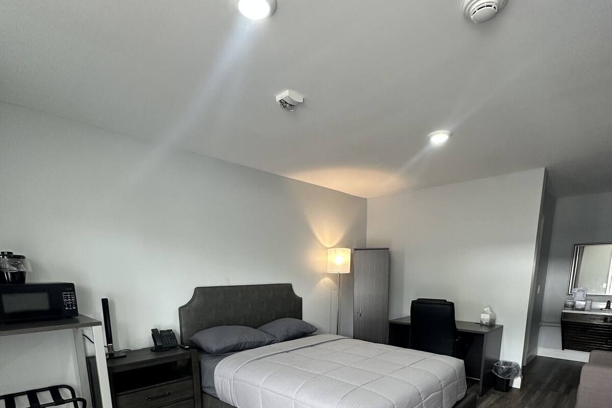 A modern bedroom with a large bed, a desk with a computer, a chair, and a wardrobe.
