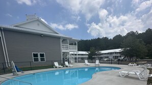 Una piscina con sillones de descanso, una zona techada y un edificio con balcón.