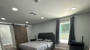 Un dormitorio con cama, mesita de noche, cómoda, puerta corredera estilo granero y ventana con cortinas.