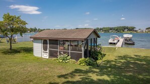 A small, single-story structure with a sloped roof, likely a gazebo or shed, situated on a grassy area near a body of water. - Beautiful 6 bedroom lake house. Pontoon available for rent (Union)