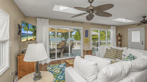 A spacious living room with a white sofa, a ceiling fan, and a view of a deck with outdoor furniture. - Beautiful 6 bedroom lake house. Pontoon available for rent (Union)