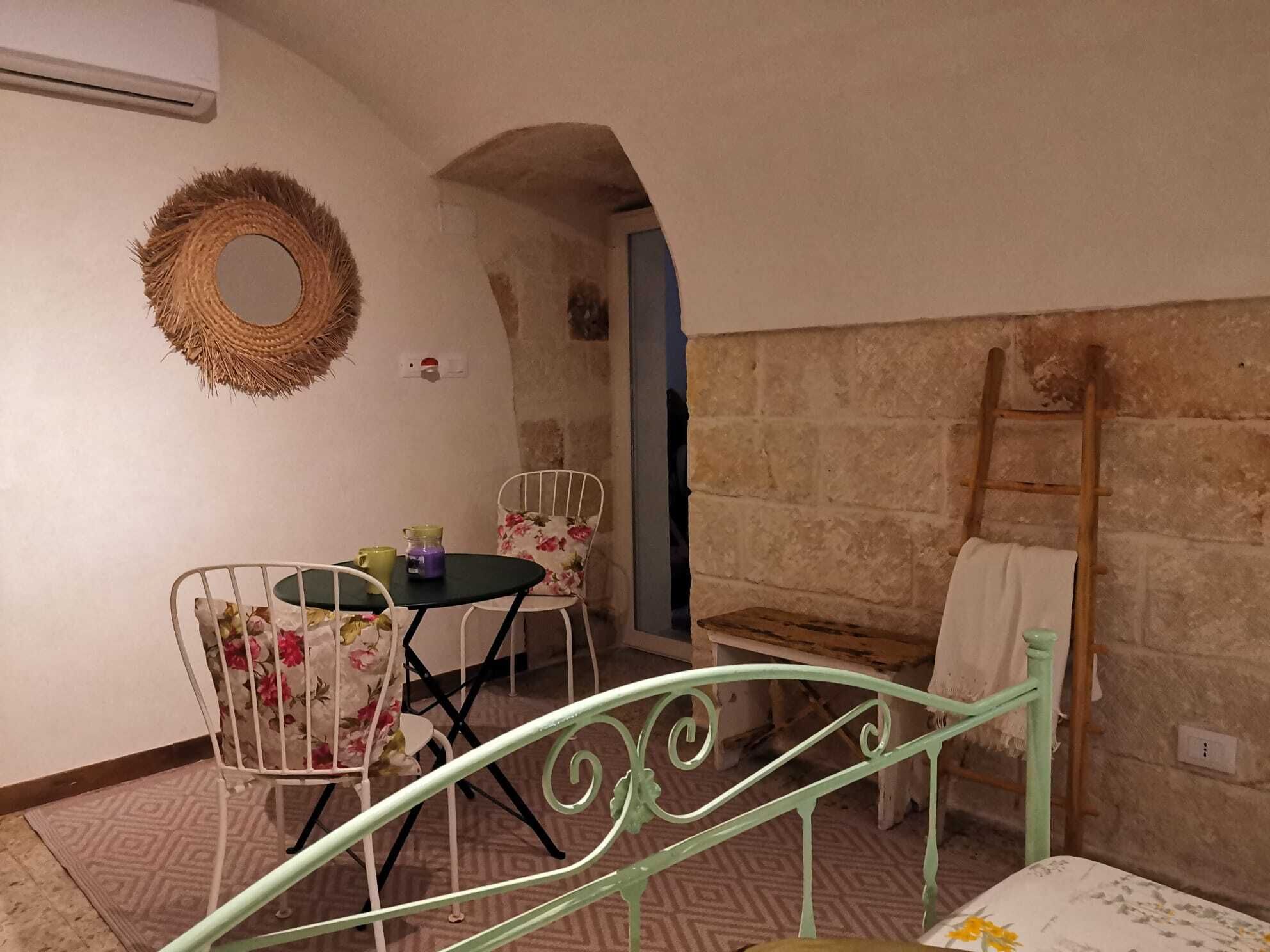 A cozy room with a metal staircase, a small table with chairs, a wicker wall hanging, and a ladder against the wall.