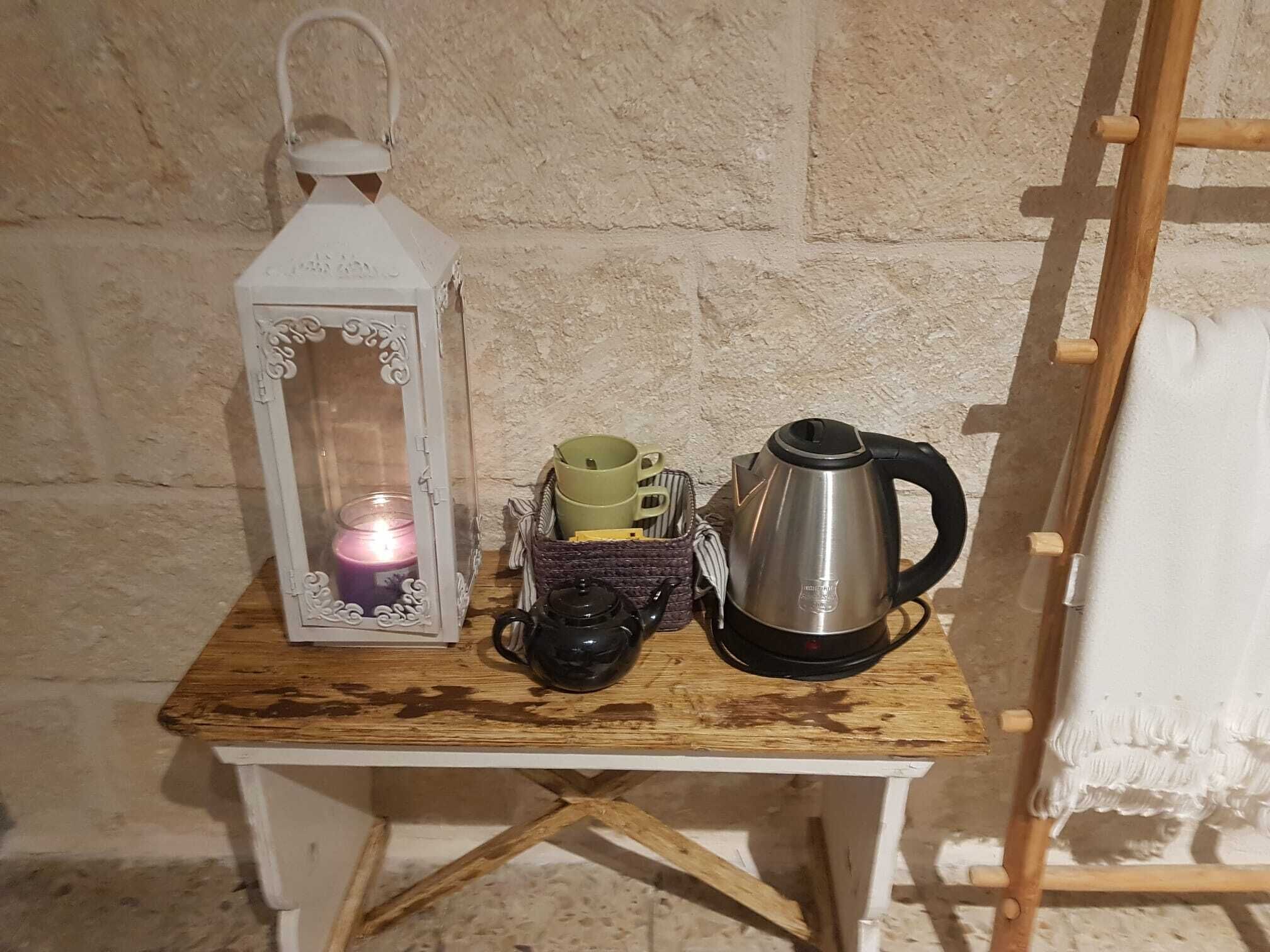 A small wooden table with a white lantern, a candle, a kettle, and a cup holder with mugs.