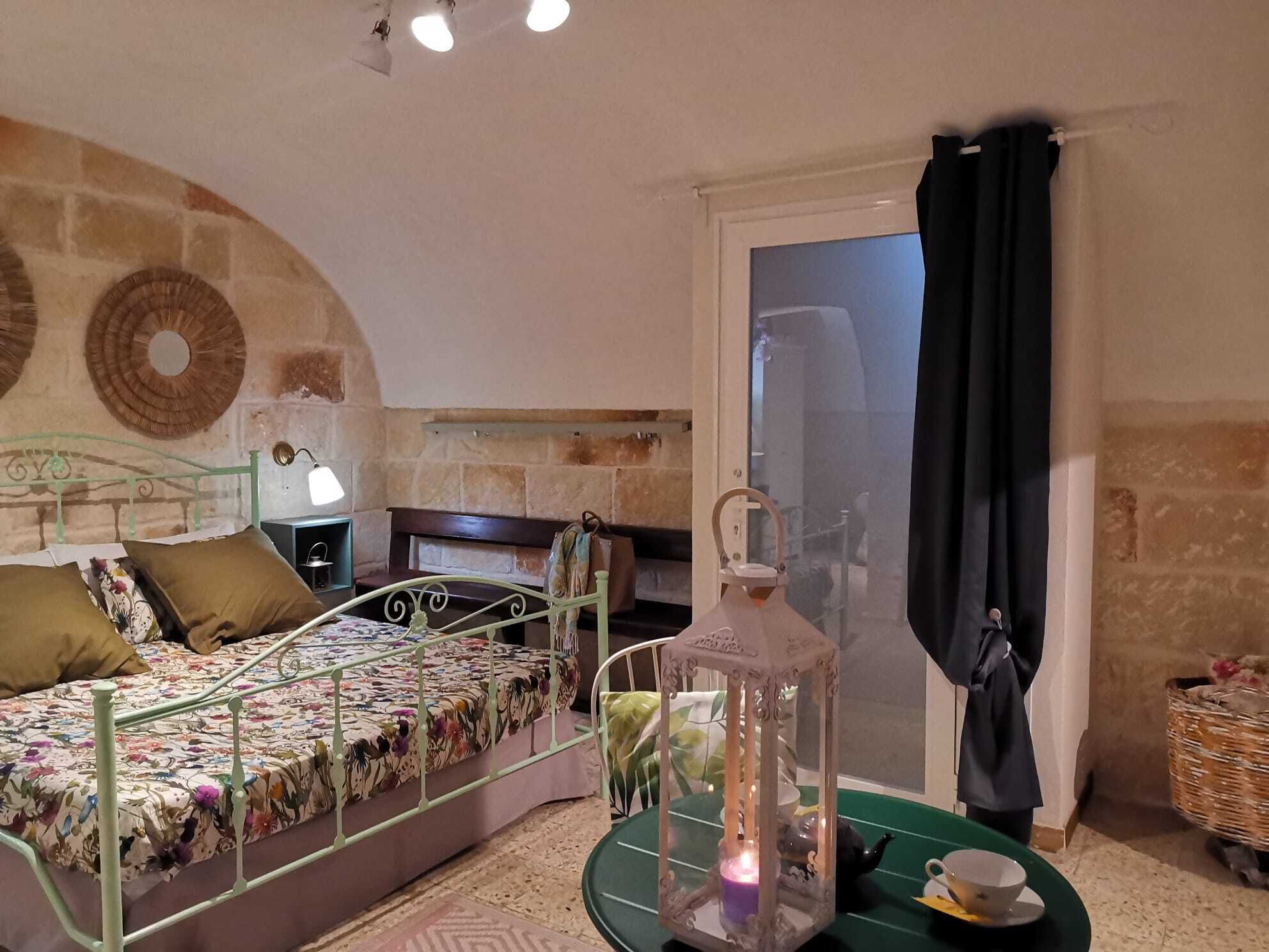 Un dormitorio con cama, mesita de noche, lámpara, farol y cesta de mimbre.