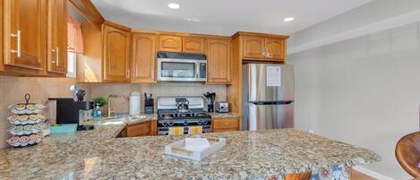 A kitchen with wooden cabinets, a stainless steel refrigerator, a microwave, and a stove.
