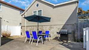 Eine Terrasse mit Tisch und Stühlen, einem Grill und einem weißen Zaun.