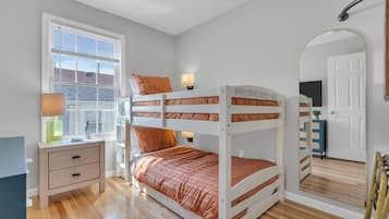 A bunk bed with a bedside table and lamp, a window with blinds, and a mirror on the wall.
