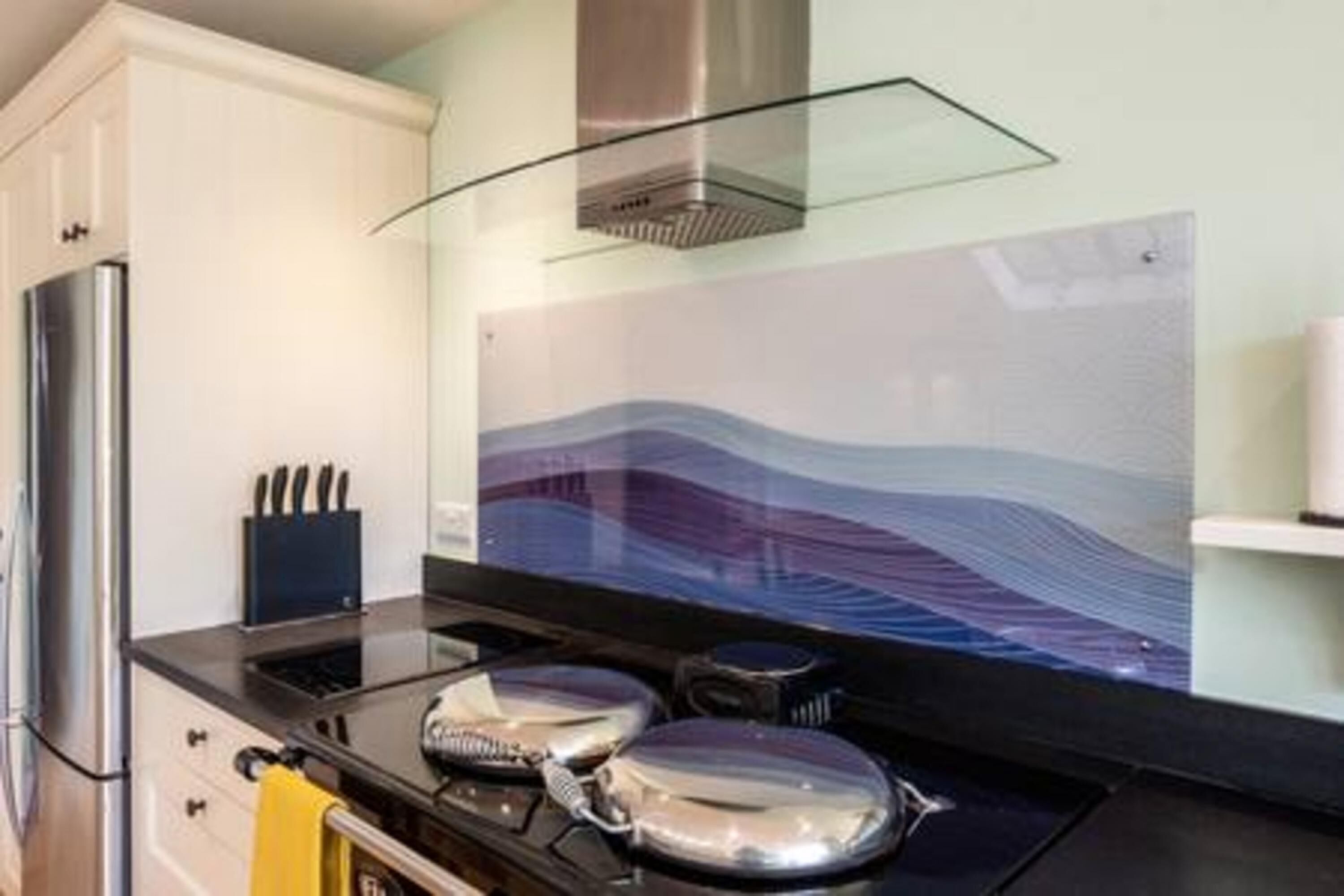 A modern kitchen with a stainless steel refrigerator, a glass backsplash, and a stove with pots and pans.