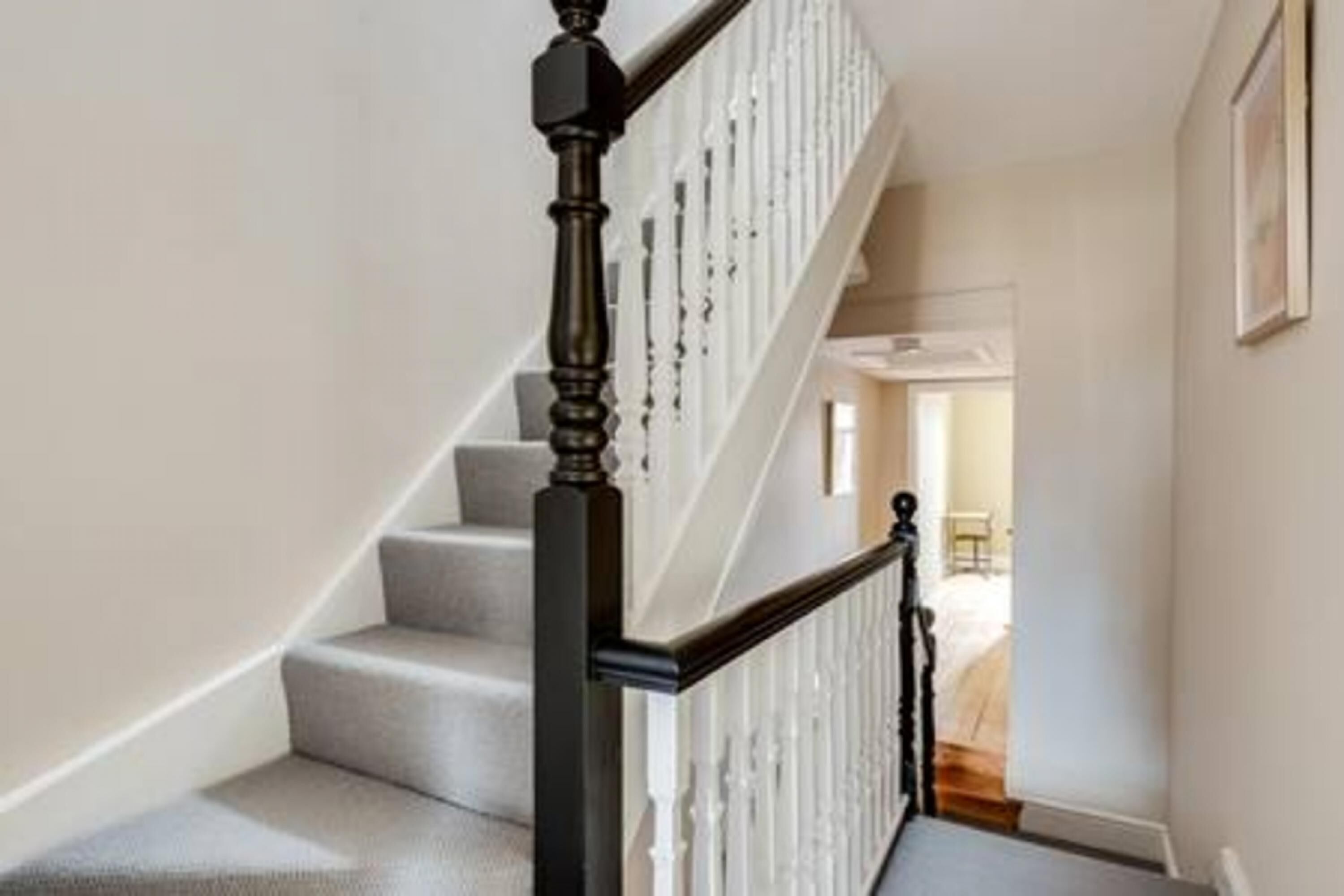 A staircase with a black handrail and white balusters, leading to a room with a white door and a framed picture on the wall.