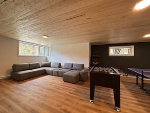 A room with a wooden ceiling, a sofa set, a foosball table, and a ping pong table.