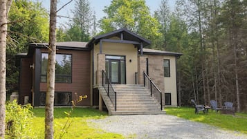 A modern two-story house with a stone facade, large windows, and a staircase leading to the entrance.