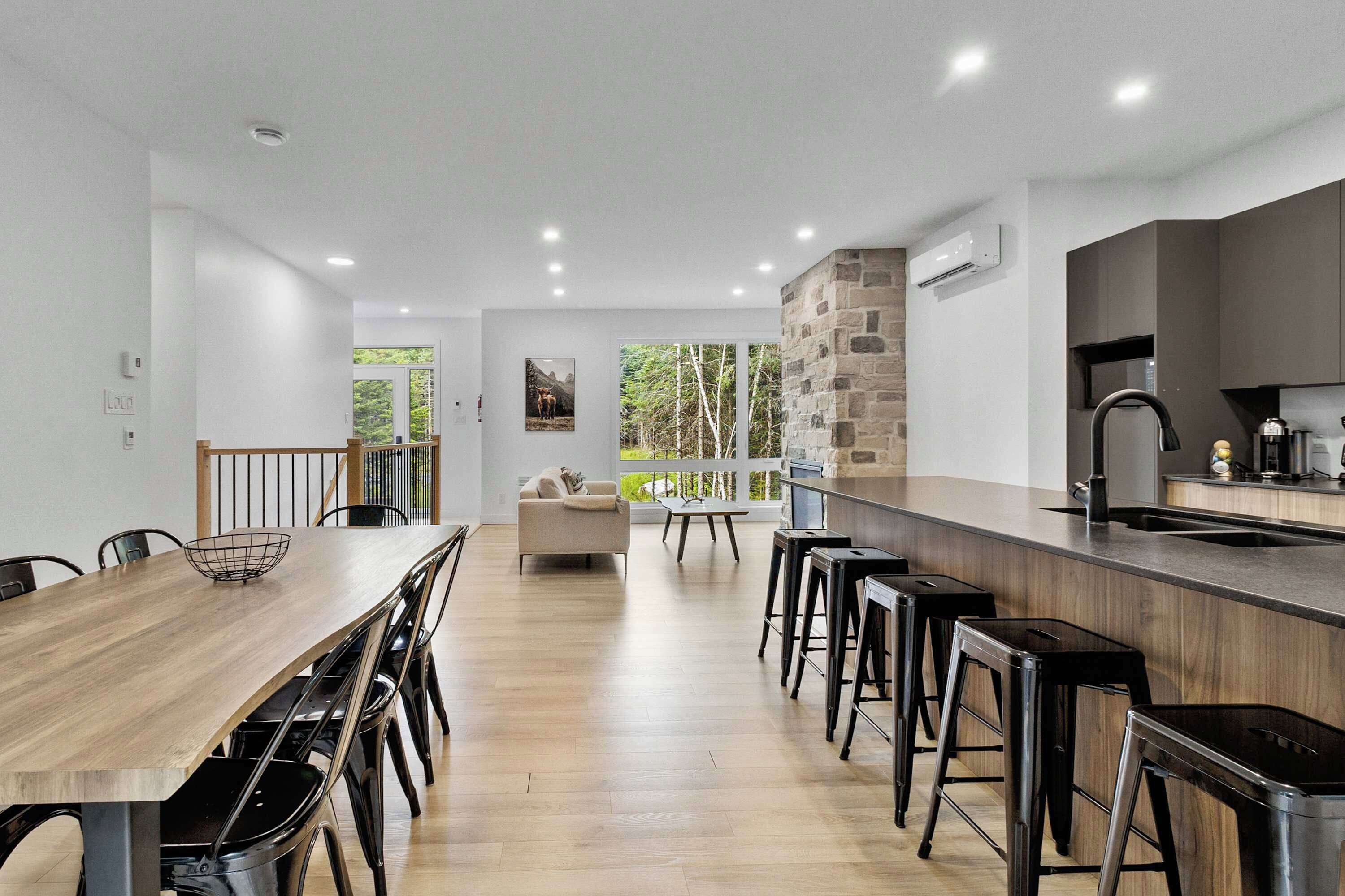 A modern kitchen with a wooden dining table, bar stools, and a stone accent wall.